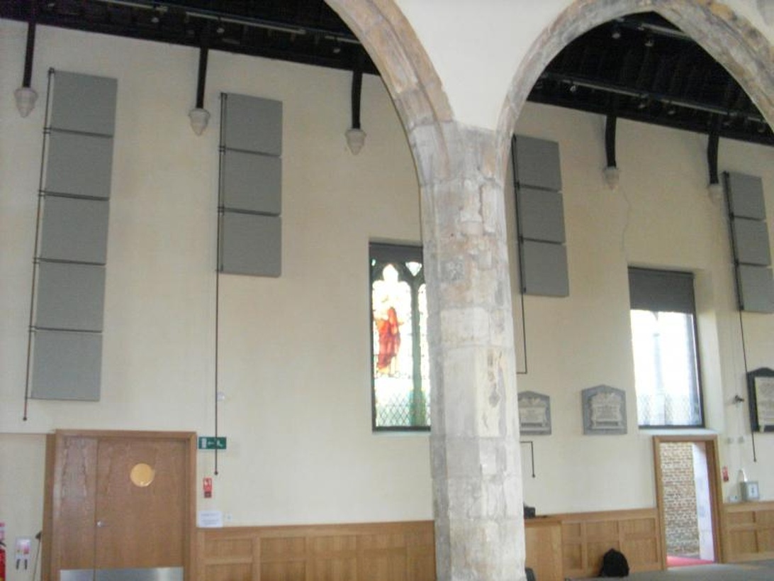Salle d'événement dans un bâtiment historique avec des arcs en pierre et des panneaux acoustiques modernes montés sur les murs.